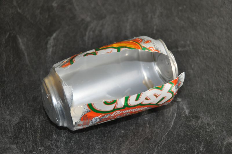 burst and crumpled Orange Crush soda can on a dark slate surface