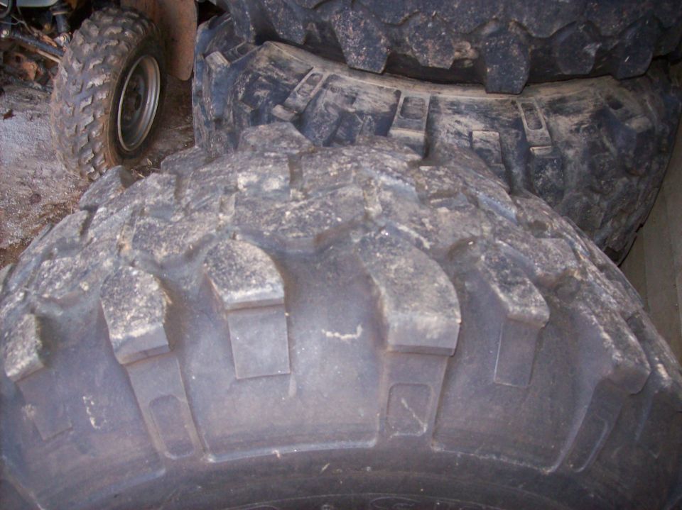 Close-up of stacked mud-terrain tire sidewall lugs with an ATV wheel behind