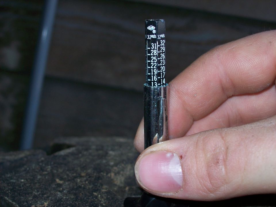 Pencil tread depth gauge held against a tire lug, 32nds scale visible
