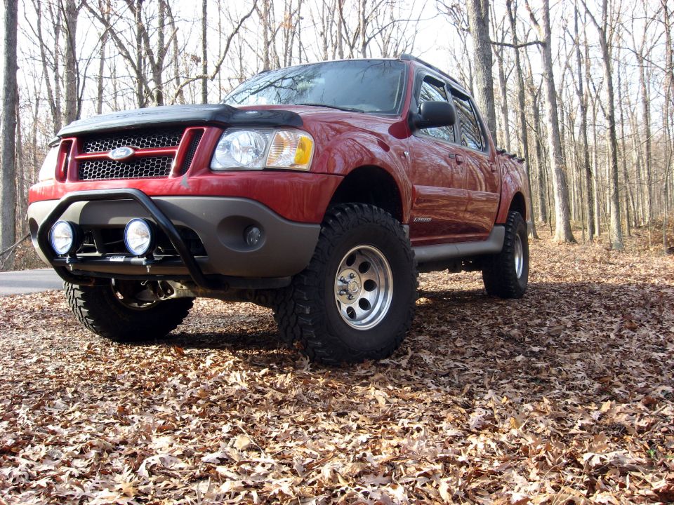 Red Ford Sport Trac pickup truck with bull bar and lights in a forest.