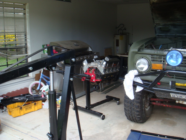 Early Ford Bronco and a V8 engine on a stand in a garage