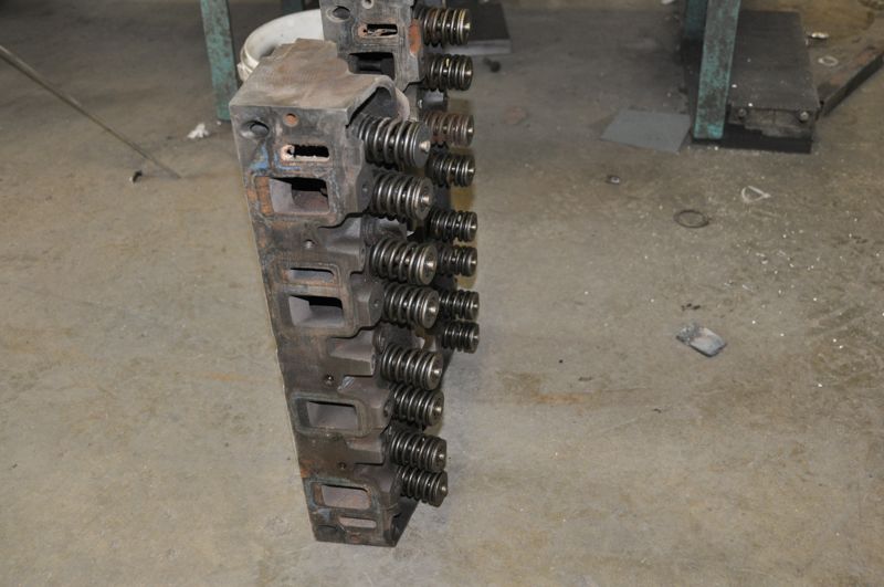 Two engine cylinder heads with valve springs visible, resting on a concrete floor