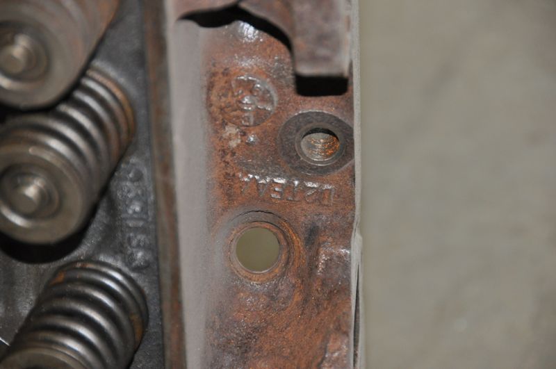 Rusty engine cylinder head with visible valve springs and stamped numbers
