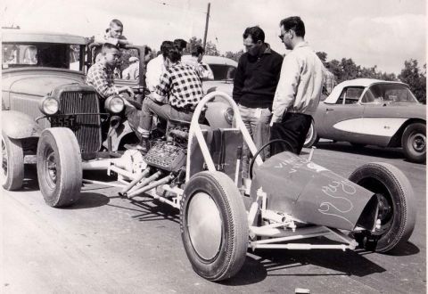 1974 Ford Ranchero - A dragster and a 1957 Chevrolet Corvette convertible are parked side-by-side, with spectators gathered around.