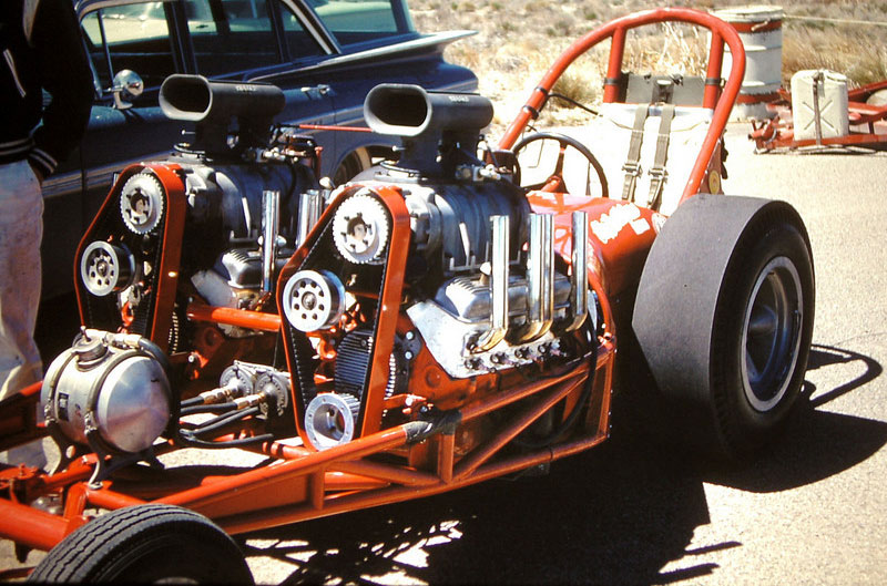 Drag racing car chassis with twin supercharged V8 engines, red frame, and large rear tire.