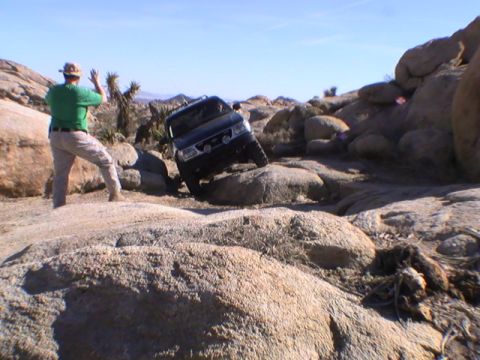 1997 Ford Ranger - A dark colored Ford Ranger is navigating a rocky, off-road trail with its front tires on large boulders. A person in a green shirt and hat…