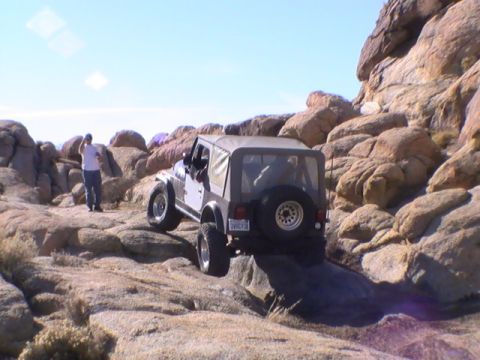 1997 Ford Ranger - A Jeep Wrangler is shown navigating a rocky, off-road trail under a clear blue sky. A person stands on the rocks to the left of the vehicle…
