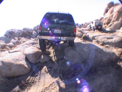 1997 Ford Ranger - The rear of a dark green SUV is shown navigating a rocky, off-road trail. The vehicle's license plate reads "4JG8690".