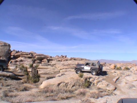 1997 Ford Ranger - A dark gray and white Jeep Wrangler is parked on a rocky, desert terrain with sparse vegetation under a clear blue sky.