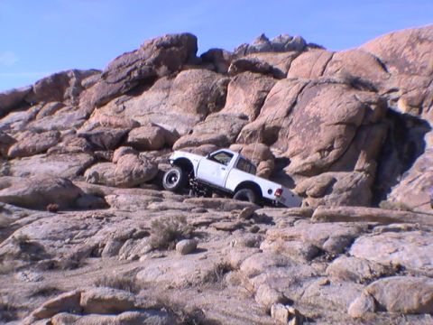 1997 Ford Ranger - A white Ford Ranger pickup truck is navigating a rocky, off-road terrain with large boulders and sparse desert vegetation under a clear blu…