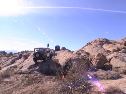 1997 Ford Ranger - Two off-road vehicles navigate a rocky, desert terrain under a bright blue sky. A person stands on top of the lead Jeep, observing the path…