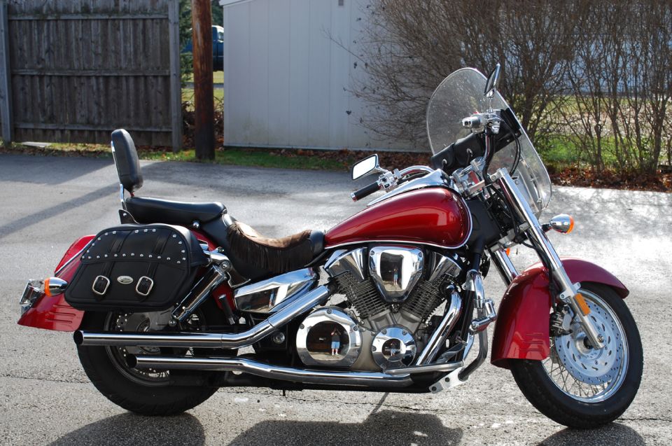 Right-side view of a red Honda VTX cruiser with windshield, chrome exhaust, and studded saddlebags