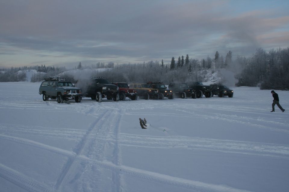 Several off-road vehicles parked in the snow with a person walking in the distance.