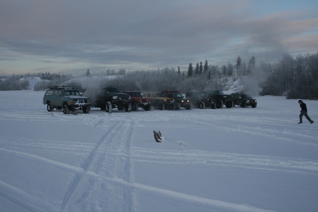 Several vehicles parked in a snowy field with a person walking in the distance