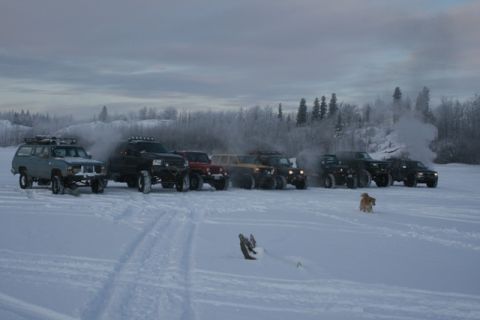 1990 Chevrolet Suburban - A convoy of off-road vehicles, including a 1990 Chevrolet Suburban, parked in a snowy, wooded area.