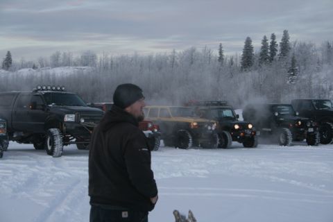 1990 Chevrolet Suburban - A group of modified off-road vehicles are gathered in a snowy landscape, with a person observing them.