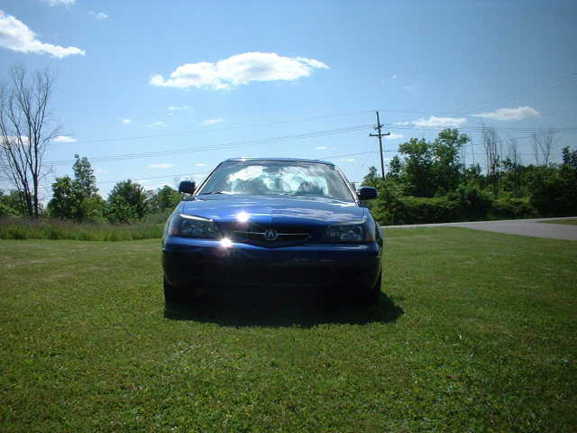 Dark blue Acura coupe photographed head-on parked on a grassy field