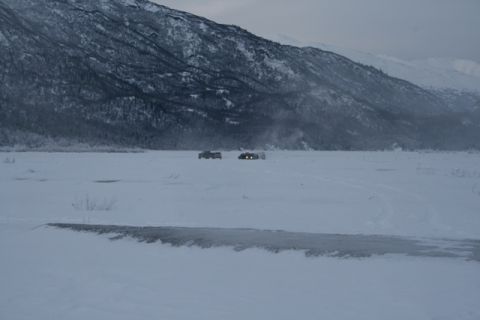 1990 Chevrolet Suburban - Two vehicles are visible in a wide, snowy expanse under a cloudy sky, with a mountain range in the distance.