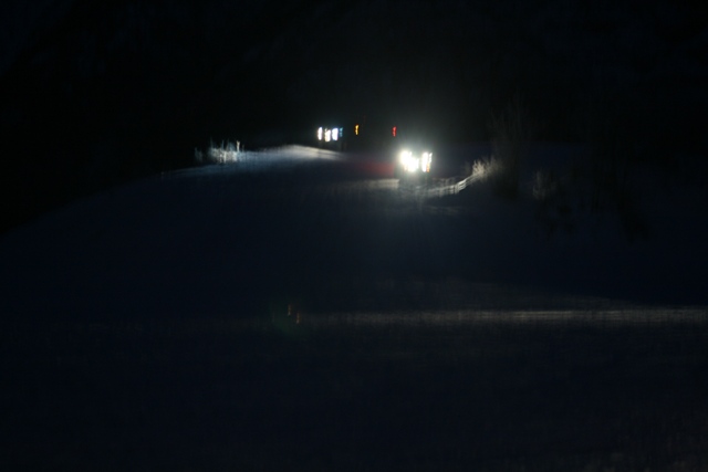 Several vehicles with headlights on drive on a snow-covered road at night