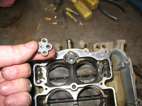 1978 Ford Bronco - A person is holding a small, four-holed metal component above a disassembled carburetor, with tools visible in the background.