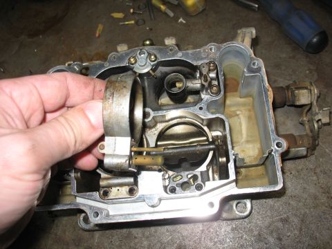 1978 Ford Bronco - Close-up of a disassembled carburetor, with a hand adjusting a linkage mechanism.