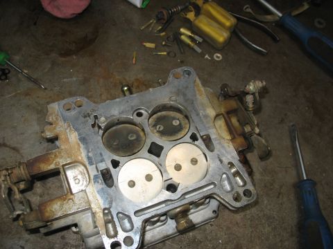 1978 Ford Bronco - A disassembled carburetor sits on a workbench next to various tools and small parts.