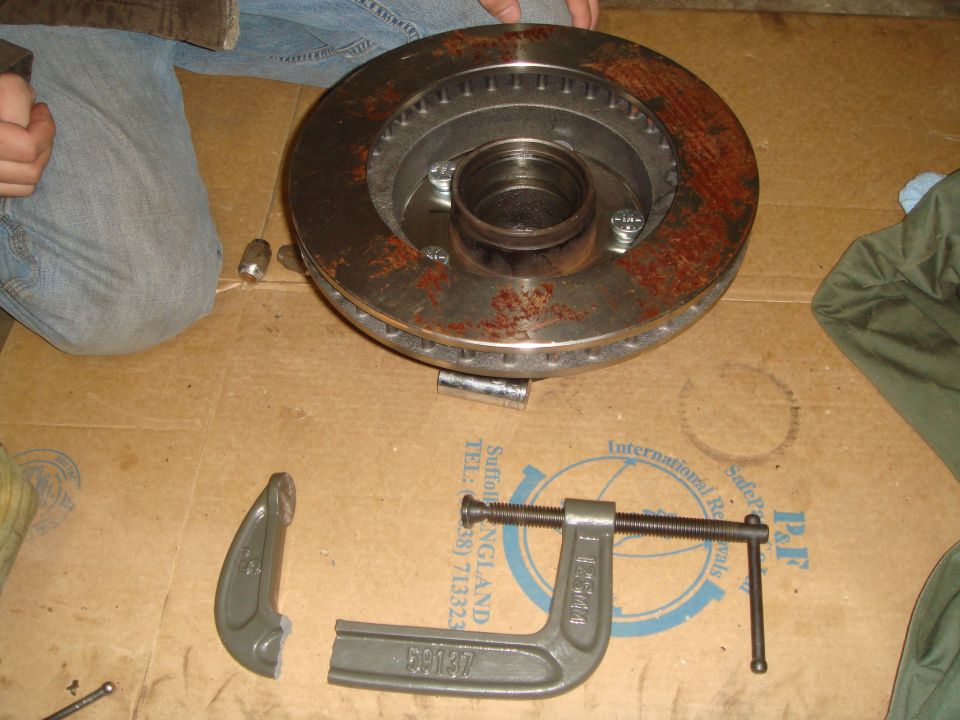 Rusty brake rotor with hub assembly and a C-clamp on a cardboard surface
