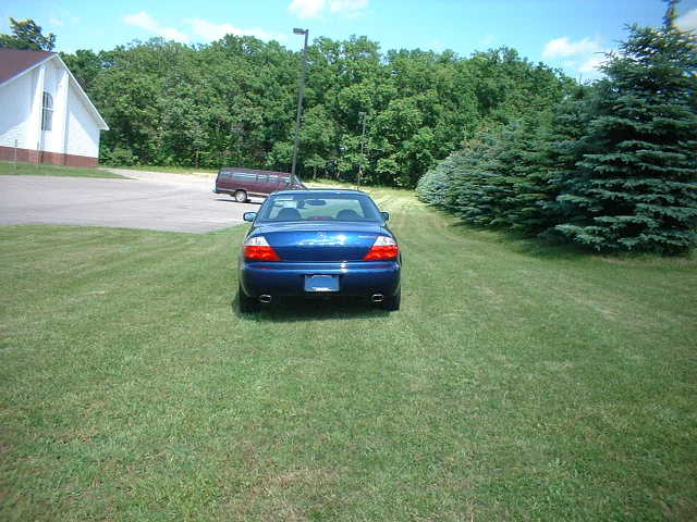 Rear view of a blue coupe with dual exhaust tips and spoiler parked on grass