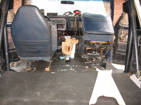 1978 Ford Bronco - The interior of a vehicle shows two blue seats, a dashboard with visible wiring, and a roll cage structure.