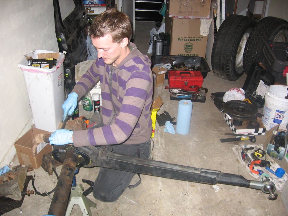 Man kneeling and working on a solid axle assembly in a garage