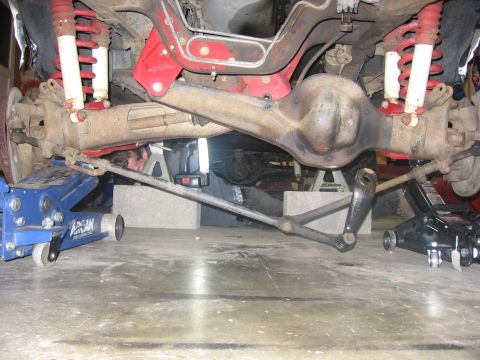1989 Ford Bronco - Photograph looking under a vehicle at an installed front axle with red coil springs and radius arms.
