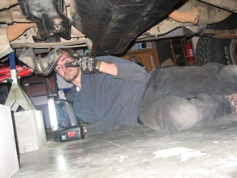 1989 Ford Bronco - Photograph of a man lying on his back working under a vehicle with a worklight.