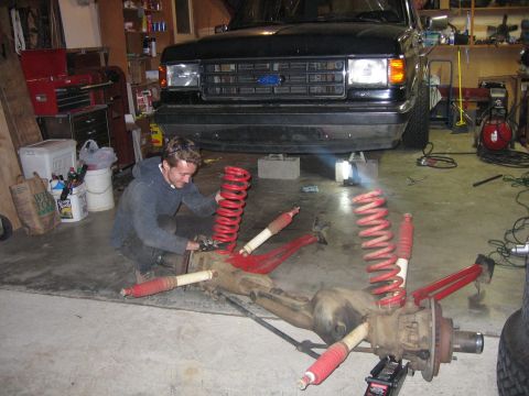 1989 Ford Bronco - Photograph of a man assembling a front axle with red coil springs and shocks before a black Ford truck.