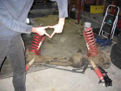 1989 Ford Bronco - Photograph of a man fitting red coil springs onto a front axle assembly on a garage floor.