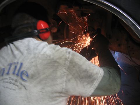 1989 Ford Bronco - Photograph of a man wearing ear protection grinding under a vehicle as sparks fly.