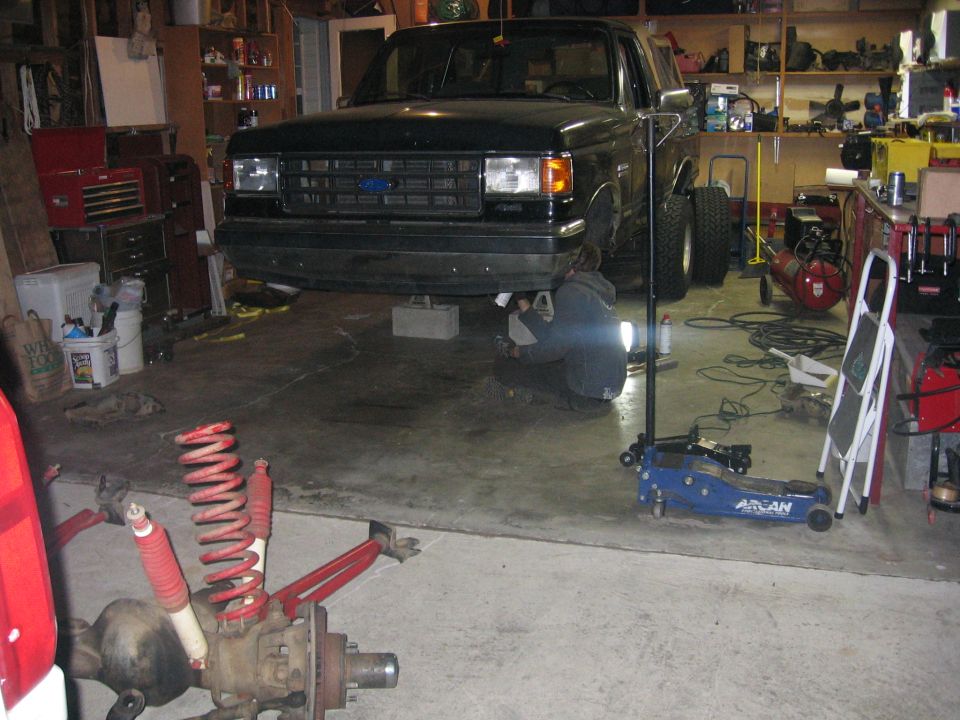 Black Ford truck raised on a stand in a home garage with tools