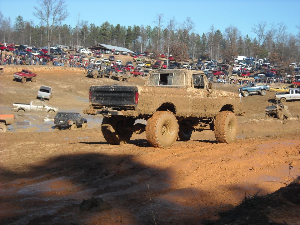 Lifted muddy pickup on large tires driving through a mud-bog course