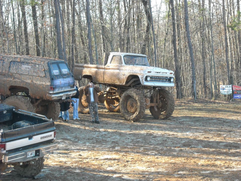 Lifted muddy pickup on huge tires parked among other trucks in the woods