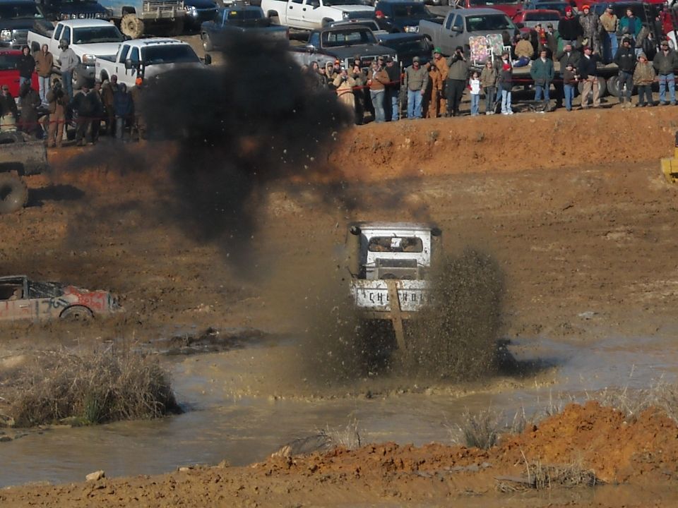 White-cab truck blasting through a mud pit with spray and exhaust smoke