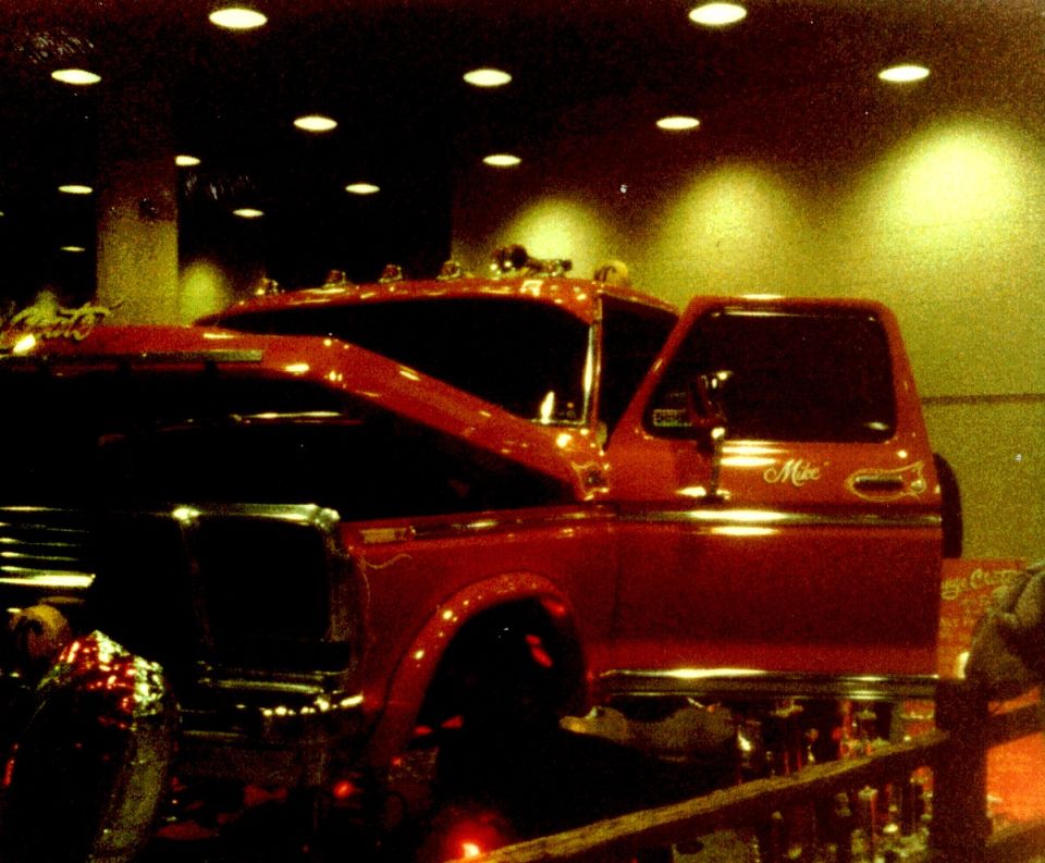Customized red pickup with cab lights and Mike script on the door at an indoor show, trophies in front