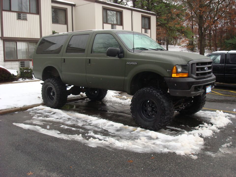 Army-green lifted Ford Excursion SUV on black wheels and mud tires in snowy parking lot