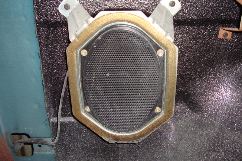 Oval automotive speaker held in a gold mounting bracket on insulation