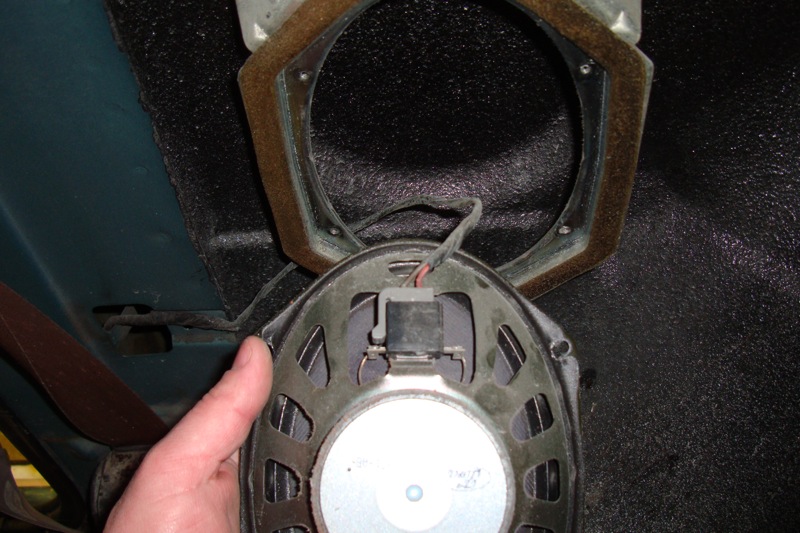 Hand holding a round speaker pulled from its bracket showing wiring
