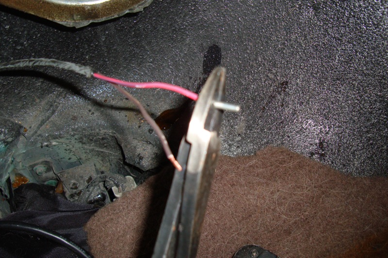 Pliers gripping wires near a metal bracket on dark carpet