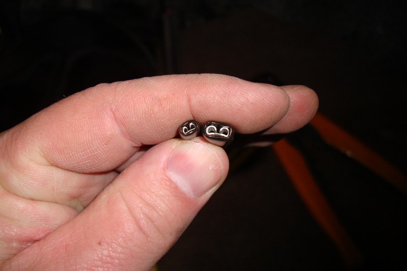 Fingers holding two small metal terminal pins or connectors