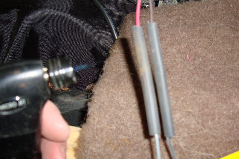 Pair of heat-shrink-wrapped wire splices with pink and bare leads on carpet