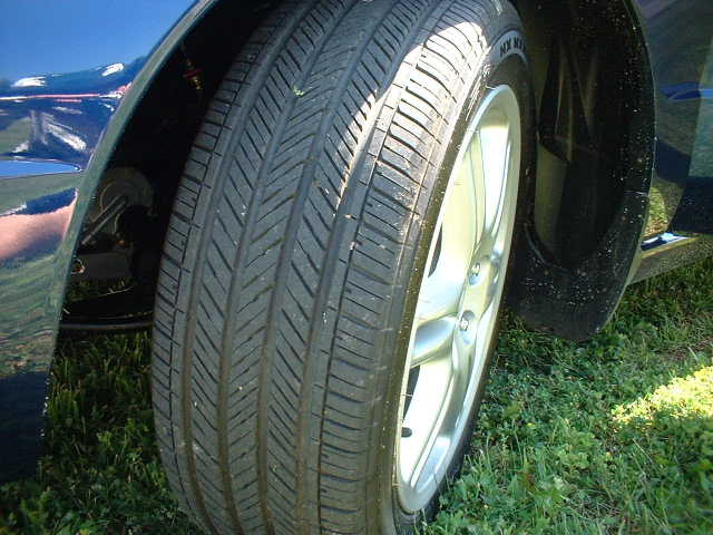 Close-up of silver five-spoke alloy wheel and all-season tire on a dark blue car parked on grass