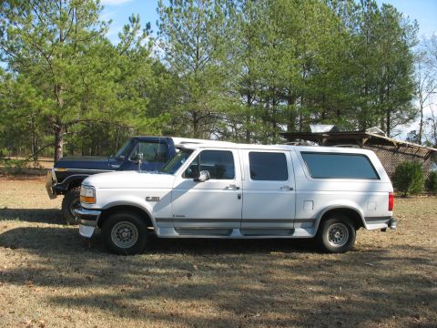 1978 Ford Bronco - Photo of a white Ford crew-cab with camper shell next to a dark Bronco, not a technical document.
