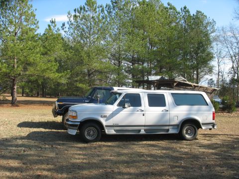 1978 Ford Bronco - Photo of a white Ford crew-cab with camper shell beside a dark Bronco, not a technical document.