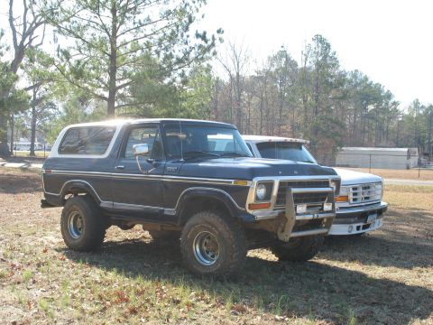1978 Ford Bronco - Photo of a lifted dark Ford Bronco and a white Ford parked side by side, not a technical document.